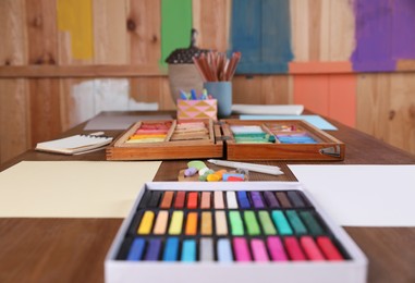 Blank sheets of paper, colorful chalk pastels and other drawing tools on wooden table indoors. Modern artist's workplace
