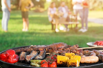 Group of friends having party outdoors, focus on barbecue grill with food