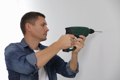 Man with drill making hole in white wall