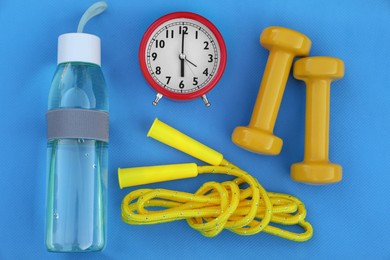 Photo of Alarm clock, skipping rope, dumbbells and bottle of water on fitness mat, flat lay. Morning exercise