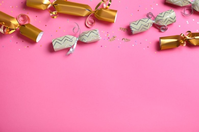 Open and closed Christmas crackers with shiny confetti on pink background, flat lay. Space for text