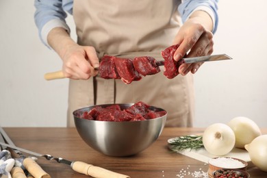 Woman stringing marinated meat on skewer at wooden table, closeup