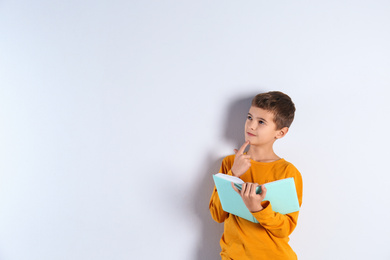 Cute little boy with book on light background, space for text