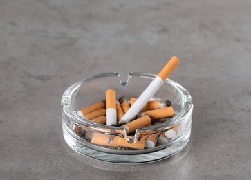 Glass ashtray with cigarette butts on grey table. Space for text