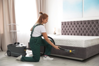 Janitor cleaning bed with professional equipment in room