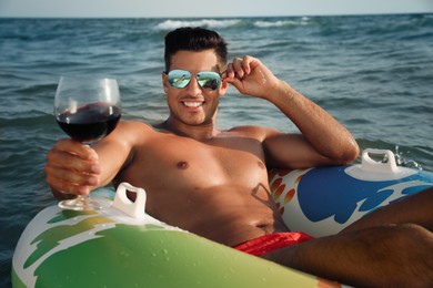 Man with glass of wine and inflatable ring resting in sea