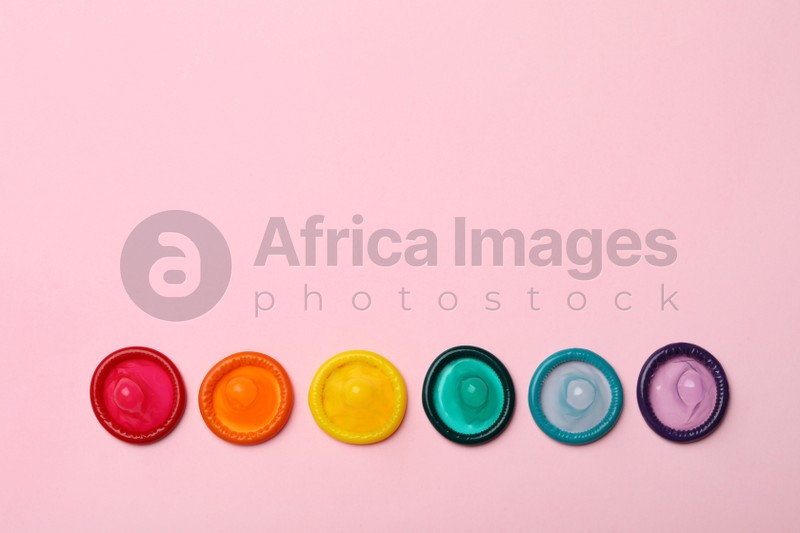 Flat lay composition with colorful condoms on pink background, space for text. LGBT concept