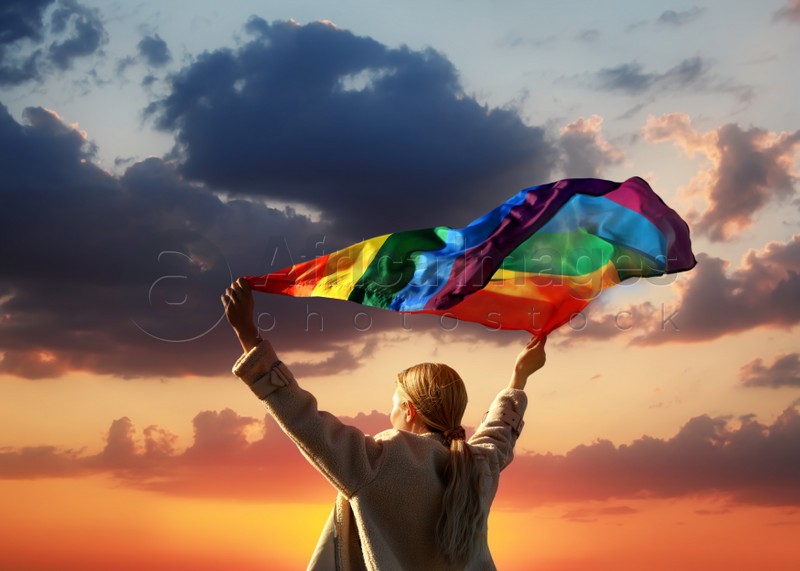 Woman with bright LGBT flag against sky at sunset