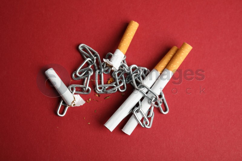 Photo of Cigarettes and chain on red background, flat lay. Quitting smoking concept