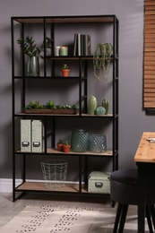Shelving with different decor, books and houseplants near gray wall in room. Interior design