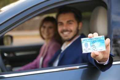 Young man holding driving license in car with passenger. Space for text