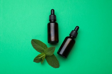 Bottles of essential oil and mint on green background, flat lay