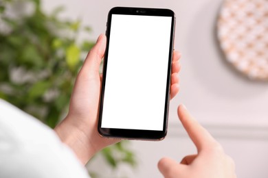 Photo of Woman holding smartphone with blank screen indoors, closeup. Mockup for design