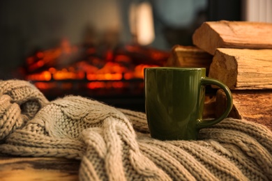 Green cup with hot drink and blanket on table against fireplace