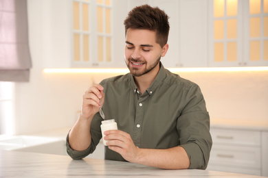 Happy young man with tasty yogurt at table in kitchen