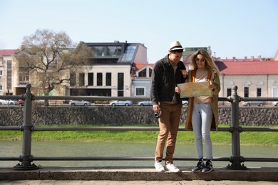Couple of tourists with map on city street near beautiful river