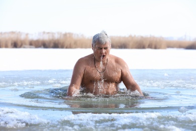 Mature man immersing in river on winter day. Baptism ritual