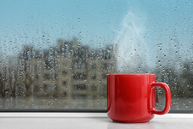 Cup of hot drink near window on rainy day