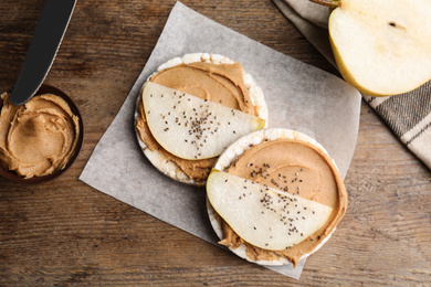Puffed rice cakes with peanut butter and pear on wooden table, flat lay