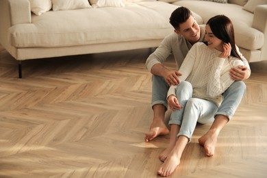 Happy couple sitting on warm floor in living room. Heating system