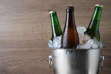 Photo of Metal bucket with bottles of beer and ice cubes on wooden background, closeup. Space for text