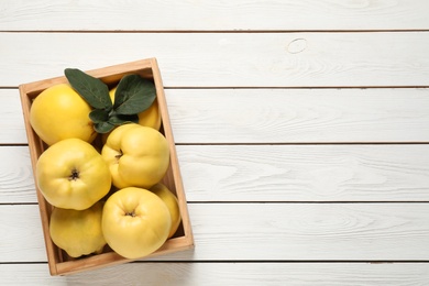 Fresh ripe organic quinces with leaves on white wooden table, top view. Space for text