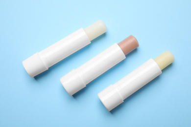 Hygienic lipsticks on light blue background, flat lay