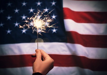 4th of July - Independence Day of USA. Woman holding burning sparkler against American flag, closeup