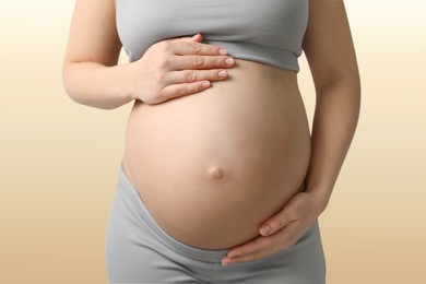 Image of Young pregnant woman touching her belly on beige background, closeup