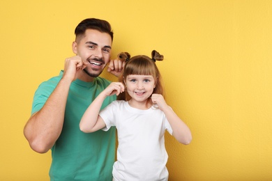 Little girl and her father flossing teeth on color background, space for text