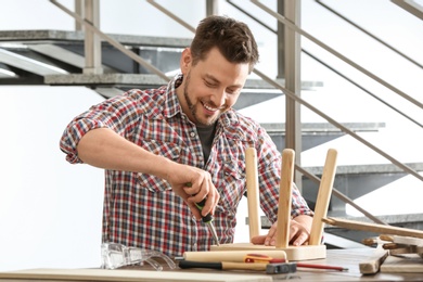 Handsome working man repairing wooden stool at table indoors