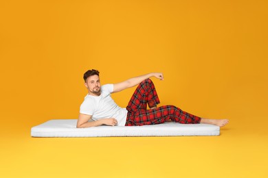Man lying on soft mattress against orange background