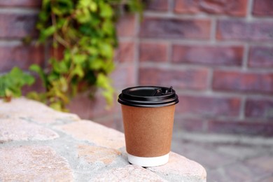 Disposable paper cup with plastic lid on stone parapet outdoors