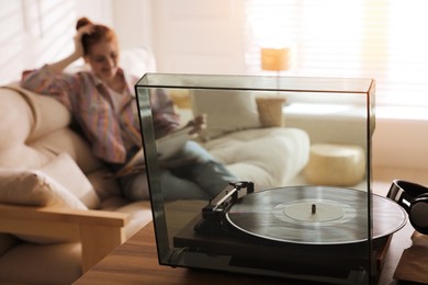 Young woman with vinyl discs in living room, focus on turntable