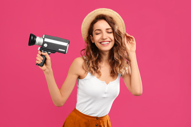 Beautiful young woman with vintage video camera on crimson background