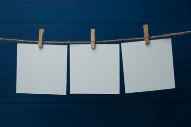 Clothespins with blank notepapers on twine against blue wooden background. Space for text
