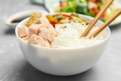 Tasty cooked rice noodles with chicken and vegetables on grey marble table, closeup