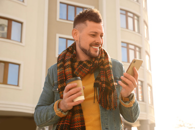 Man with cup of coffee and smartphone on city street in morning