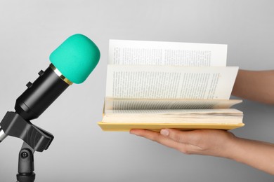 Woman making ASMR sounds with microphone and book on grey background, closeup