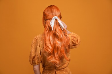 Beautiful woman with long orange hair on color background, back view