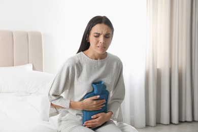Woman using hot water bottle to relieve abdominal pain on bed at home