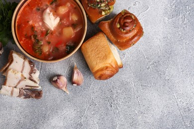 Photo of Delicious borsch served with pampushky and salo on grey textured table, flat lay and space for text. Traditional Ukrainian cuisine
