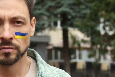 Photo of Sad man with drawings of Ukrainian flag on face outdoors, closeup. Space for text