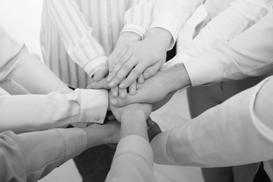 People holding hands together in office, closeup. Black and white effect