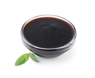 Photo of Glass bowl with balsamic glaze and basil leaves on white background