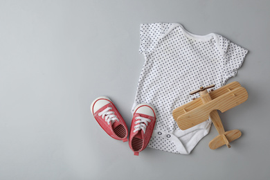 Child's shoes, bodysuit and wooden airplane on grey background, flat lay with space for text
