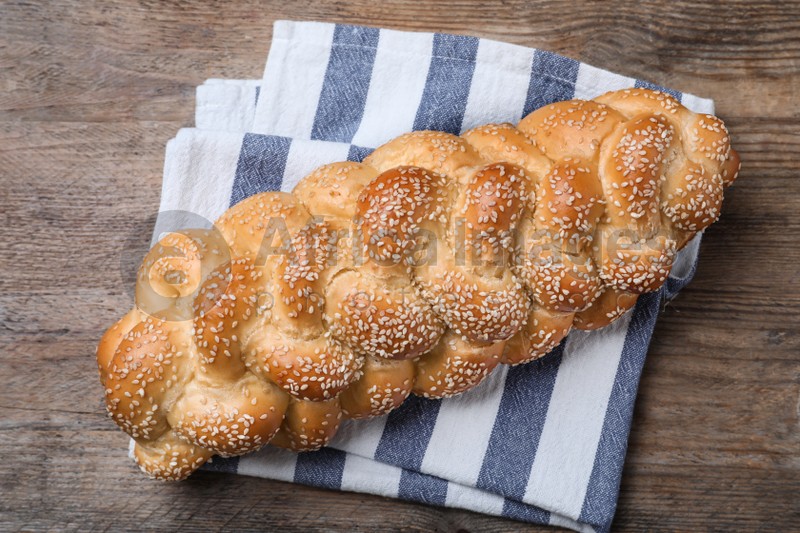 Homemade braided bread with sesame seeds on wooden table, top view. Traditional Shabbat challah