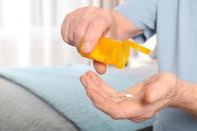 Senior man pouring pills from bottle into hand indoors, closeup