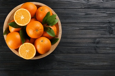 Delicious ripe oranges in bowl on black wooden table, top view. Space for text