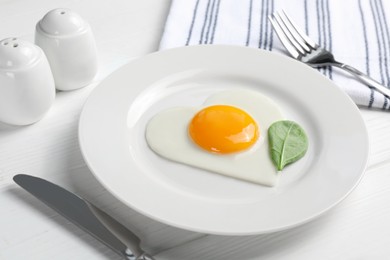 Romantic breakfast with heart shaped fried egg on white wooden table, closeup